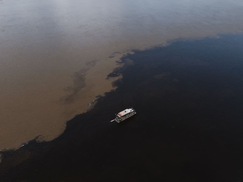 A boat navigating the Meeting of Waters, where the black Rio Negro and brown Solimões River flow side by side without mixing. A boat navigating the Meeting of Waters, where the black Rio Negro and brown Solimões River flow side by side without mixing.