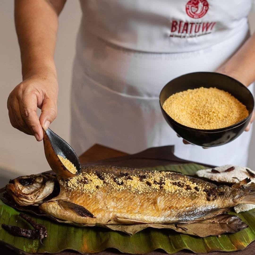 Close-up of a person sprinkling manioc flour onto a roasted fish dish served on a banana leaf. Close-up of a person sprinkling manioc flour onto a roasted fish dish served on a banana leaf.