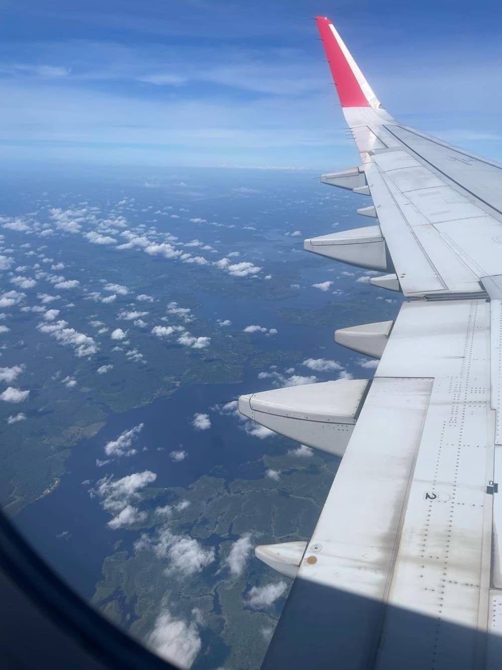 View from an airplane window looking out over the wing towards the Amazon clouds and landscape below. View from an airplane window looking out over the wing towards the Amazon clouds and landscape below.