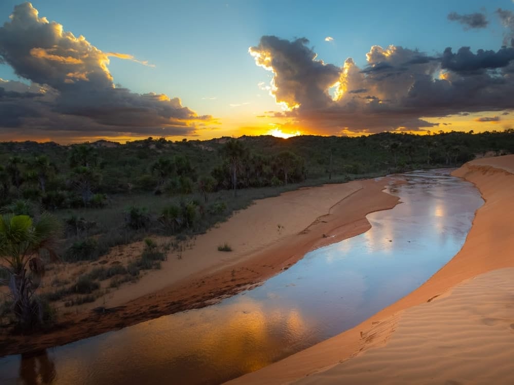 A calm river flowing through wide sandy areas and rugged cliffs during sunset, reflecting the region's geological past A calm river flowing through wide sandy areas and rugged cliffs during sunset, reflecting the region's geological past