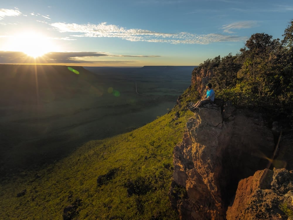 A traveler sits on a cliff edge enjoying the sunset over the vast savanna landscape of Jalapão State Park. A traveler sits on a cliff edge enjoying the sunset over the vast savanna landscape of Jalapão State Park.