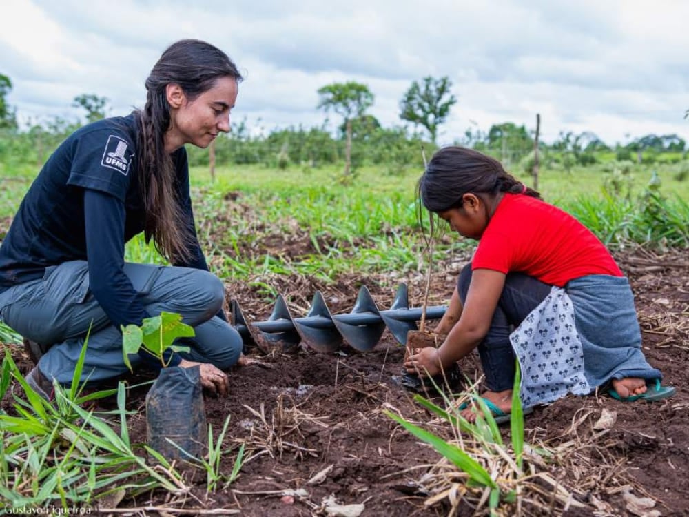 A woman and a young girl kneeling in the dirt to plant a tree sapling in the Pantanal wetlands. A woman and a young girl kneeling in the dirt to plant a tree sapling in the Pantanal wetlands.