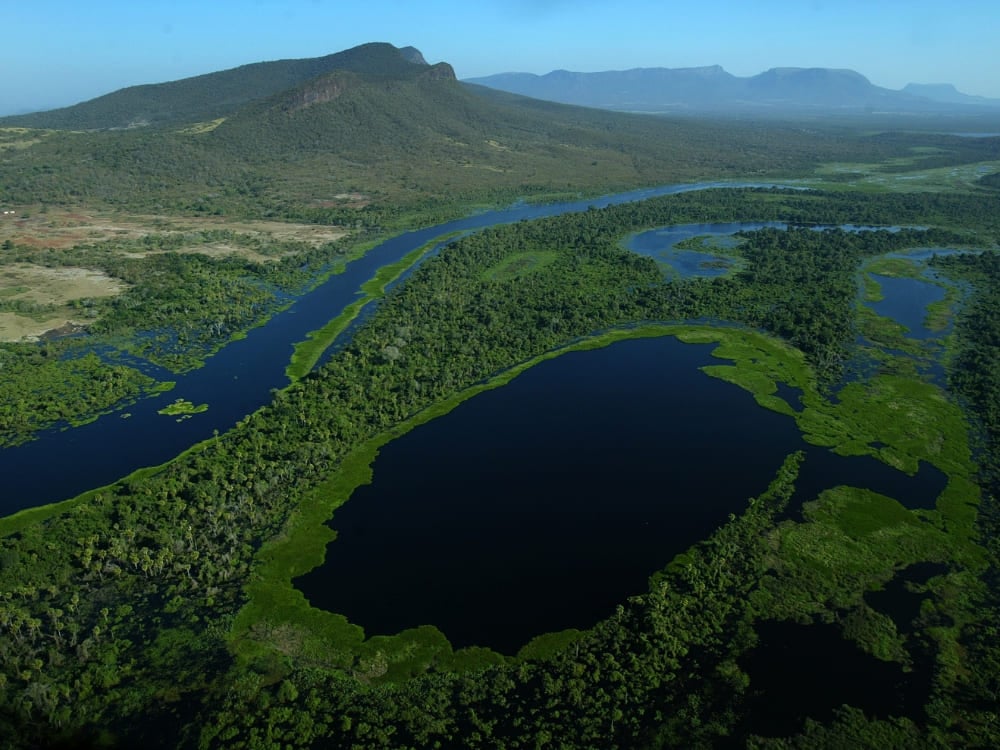 Aerial view of a deep blue river winding through the vast green plains of the region where is the Pantanal located. Aerial view of a deep blue river winding through the vast green plains of the region where is the Pantanal located.