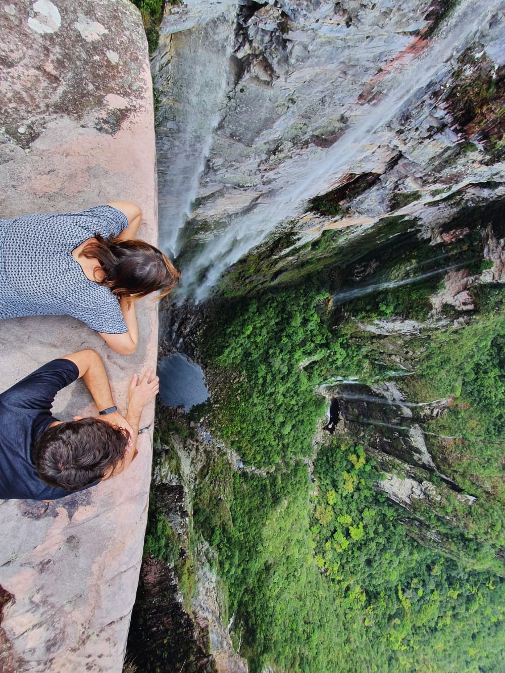 Two hikers look down a steep cliff edge at a lush green valley while trekking the iconic Vale do Pati route. Two hikers look down a steep cliff edge at a lush green valley while trekking the iconic Vale do Pati route.