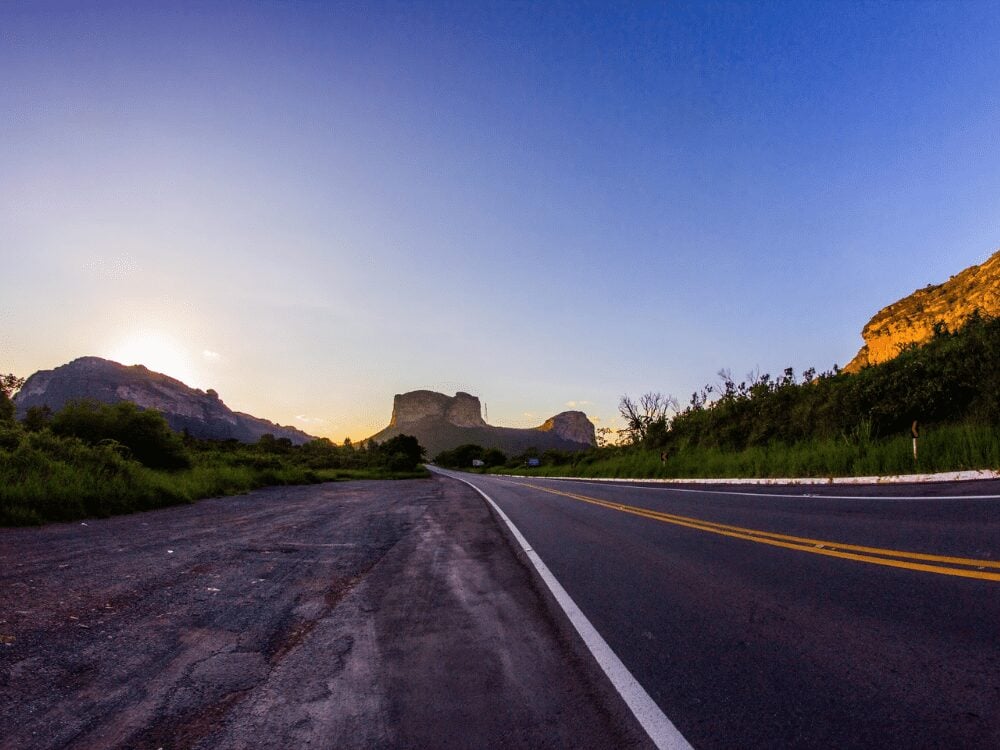 An empty paved road leads directly toward the iconic Morro do Pai Inácio mountain under a clear blue sky at dusk. An empty paved road leads directly toward the iconic Morro do Pai Inácio mountain under a clear blue sky at dusk.