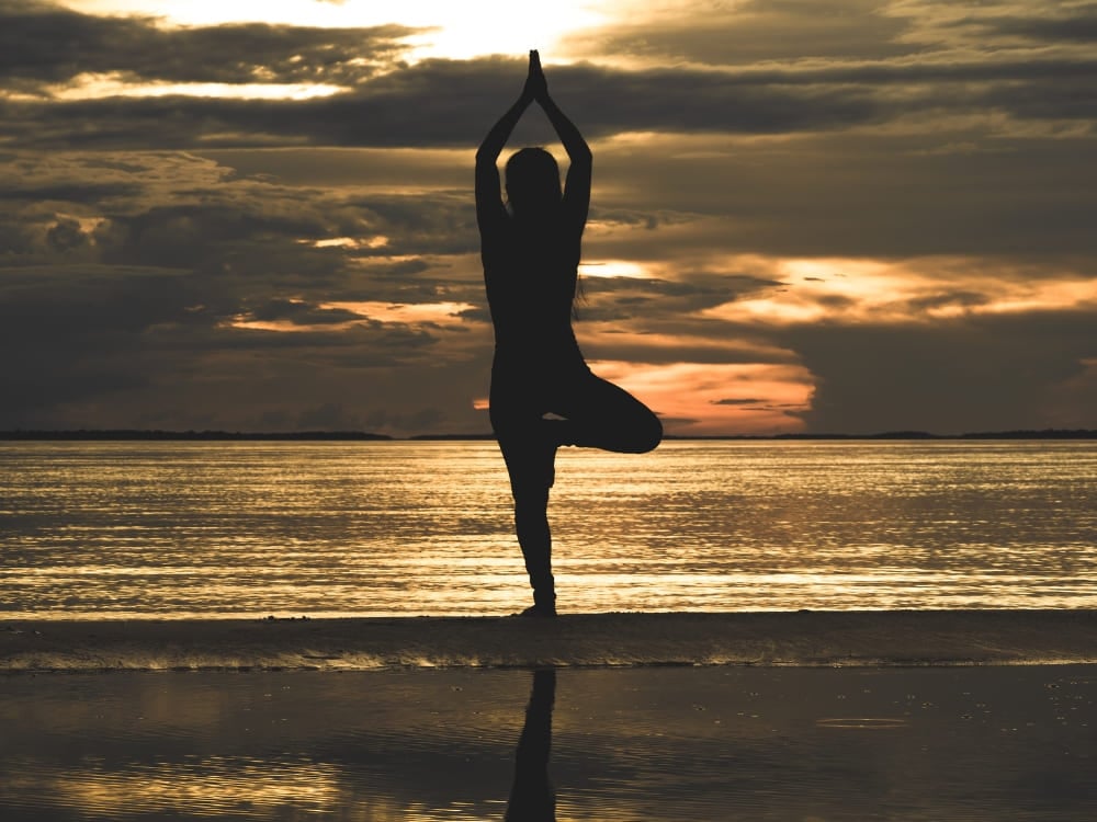 Silhouette of a person doing a yoga tree pose on an Amazon river beach at sunset. Silhouette of a person doing a yoga tree pose on an Amazon river beach at sunset.