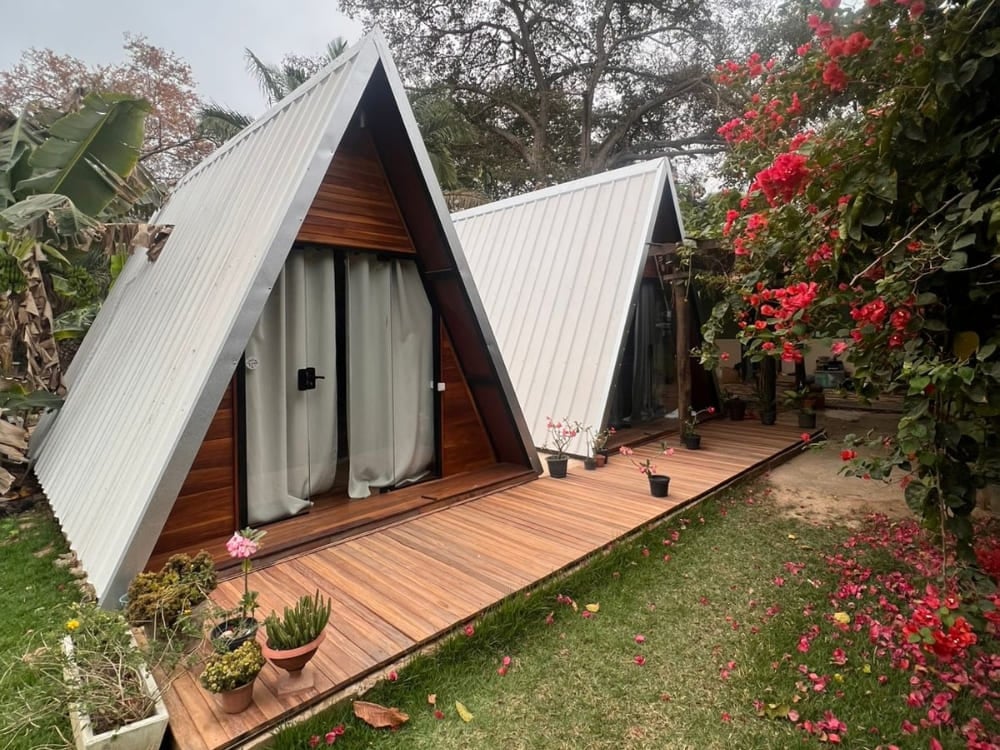 Two rustic A-frame wooden chalets sit at Berço Pantaneiro in Porto Jofre, surrounded by bright pink flowers. Two rustic A-frame wooden chalets sit at Berço Pantaneiro in Porto Jofre, surrounded by bright pink flowers.