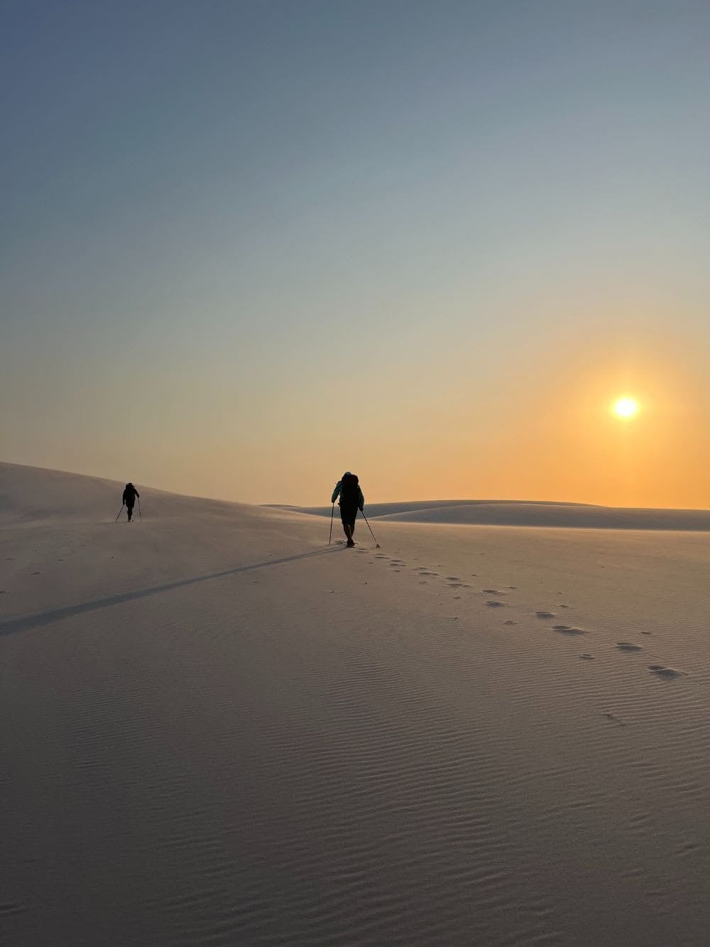 Silhouetted people walk across the sand dunes of Lençóis Maranhenses at sunset. Silhouetted people walk across the sand dunes of Lençóis Maranhenses at sunset.