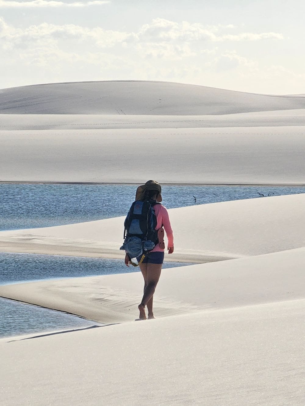 A traveler carrying a backpack walks barefoot along the shoreline of a peaceful lagoon in Santo Amaro. A traveler carrying a backpack walks barefoot along the shoreline of a peaceful lagoon in Santo Amaro.