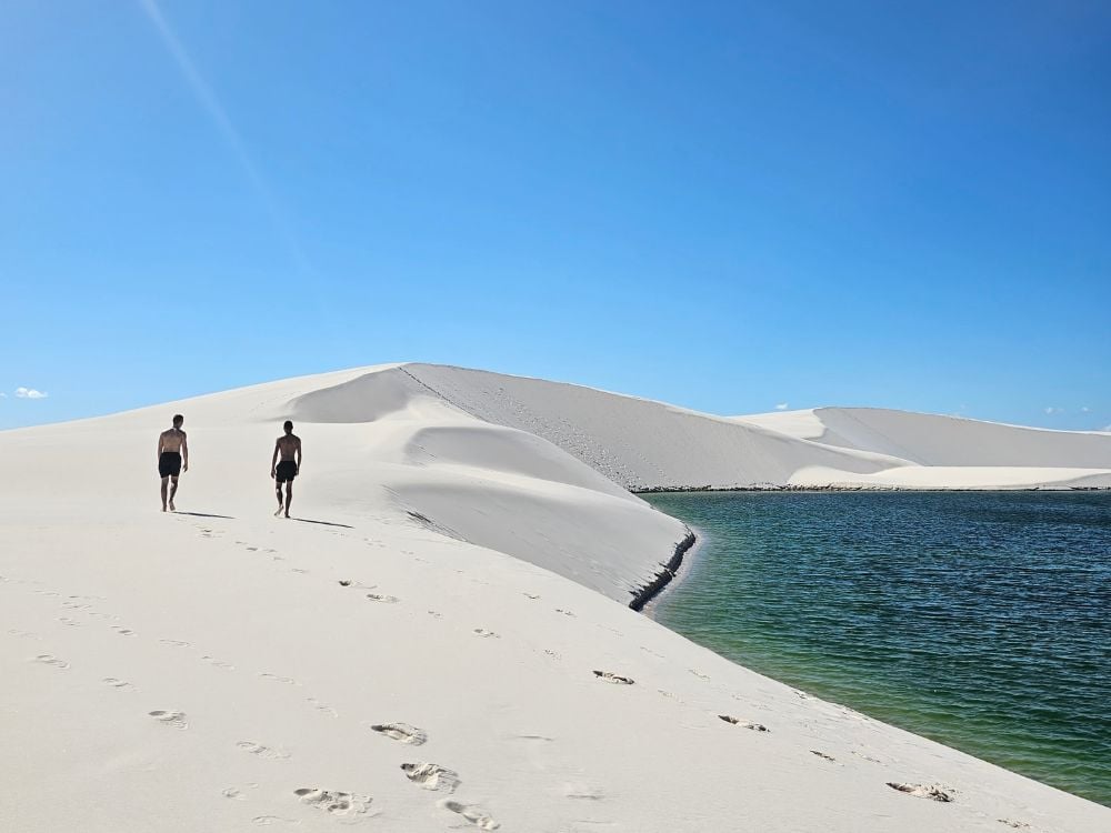 A backpacker walks across the vast white sand dunes of Lençóis Maranhenses National Park under a cloudy sky. A backpacker walks across the vast white sand dunes of Lençóis Maranhenses National Park under a cloudy sky.