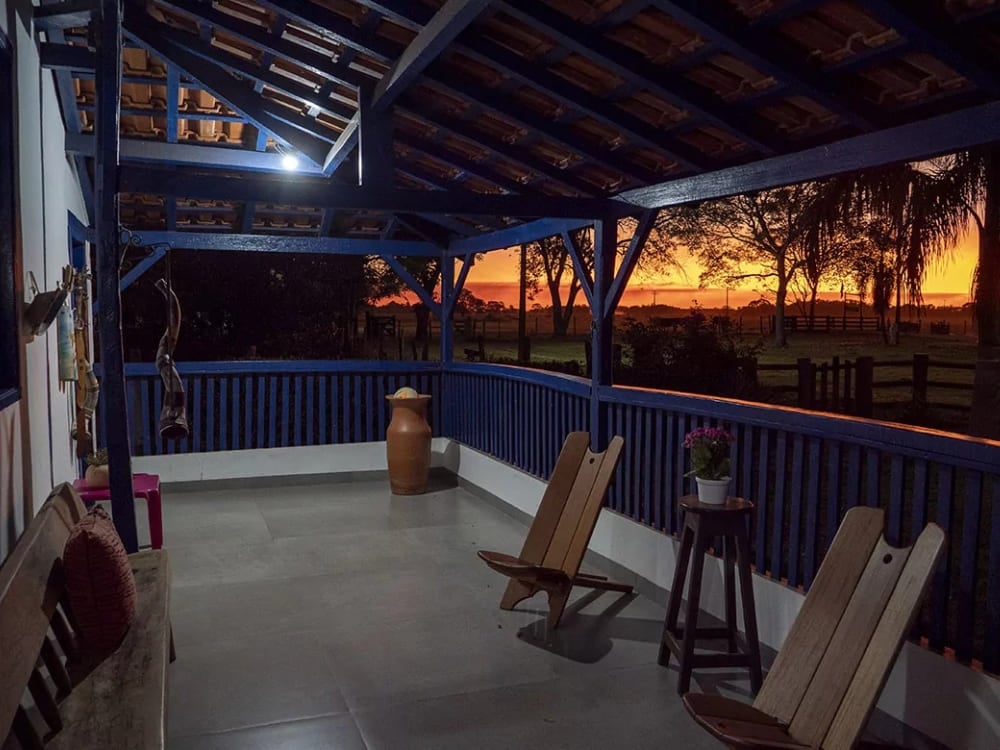 Wooden chairs rest on the blue-painted veranda of the historic Pequi farmhouse lodge during a vibrant Pantanal sunset. Wooden chairs rest on the blue-painted veranda of the historic Pequi farmhouse lodge during a vibrant Pantanal sunset.