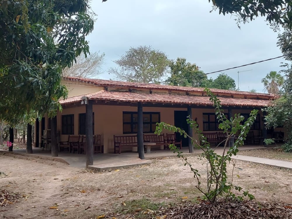 The simple and functional rustic farm architecture of Pouso Alegre lodge is shaded by large green trees. The simple and functional rustic farm architecture of Pouso Alegre lodge is shaded by large green trees.