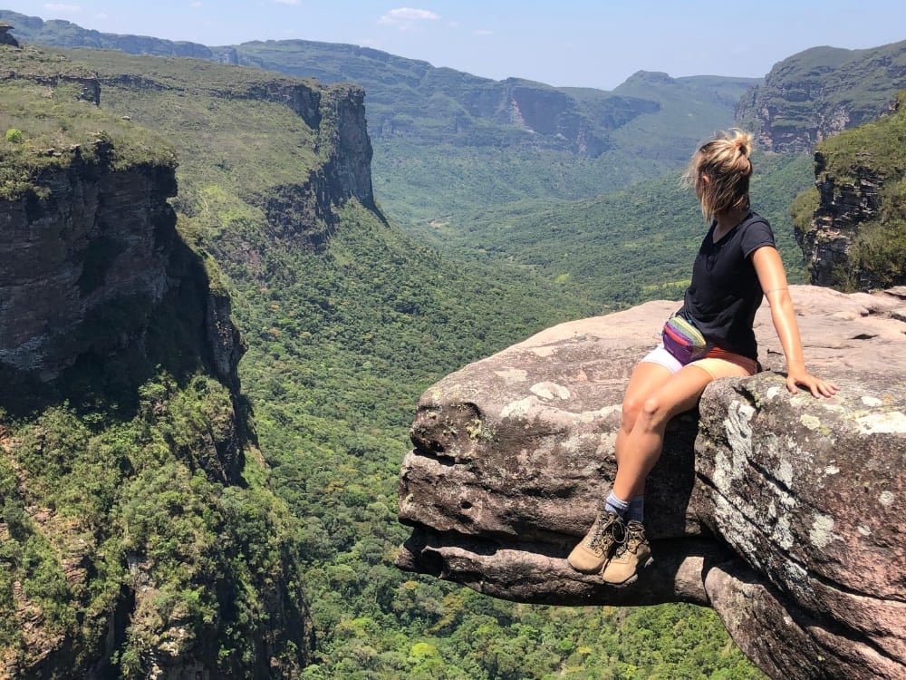 Woman hiker resting on a rocky cliff edge, overlooking a vast, lush green canyon and distant plateaus during an ecotourism adventure. Woman hiker resting on a rocky cliff edge, overlooking a vast, lush green canyon and distant plateaus during an ecotourism adventure.