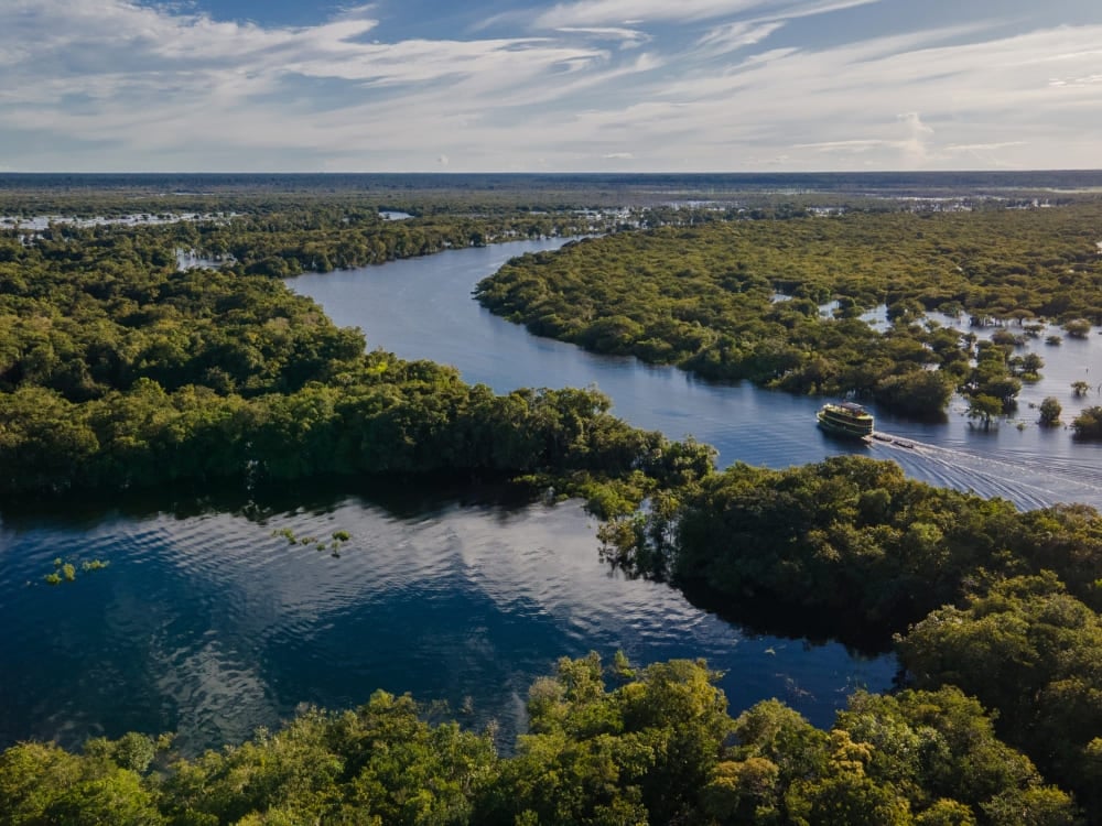Aerial view of a tour boat navigating a winding river through the lush green landscape of the Amazon. Aerial view of a tour boat navigating a winding river through the lush green landscape of the Amazon.