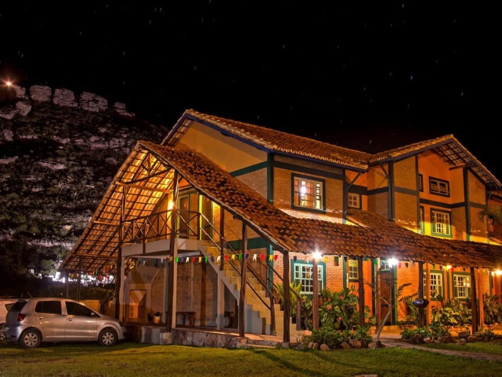 Rustic exterior of Pousada Monte Azul in Mucugê illuminated at night under a dark sky. Rustic exterior of Pousada Monte Azul in Mucugê illuminated at night under a dark sky.