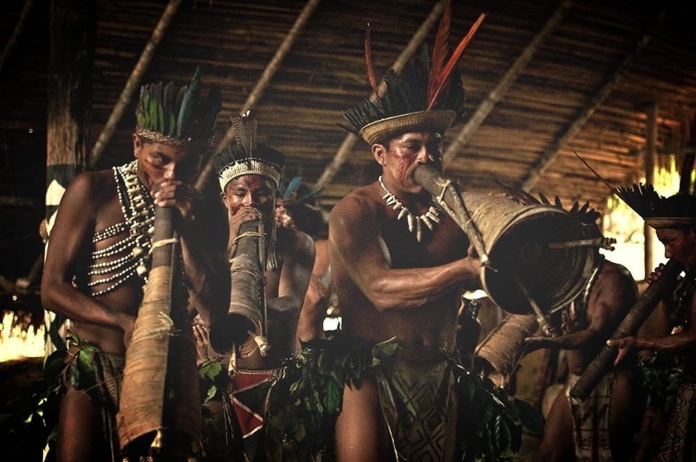 A group of indigenous people in the Amazon playing traditional long wind instruments and drums during a cultural ritual. A group of indigenous people in the Amazon playing traditional long wind instruments and drums during a cultural ritual.