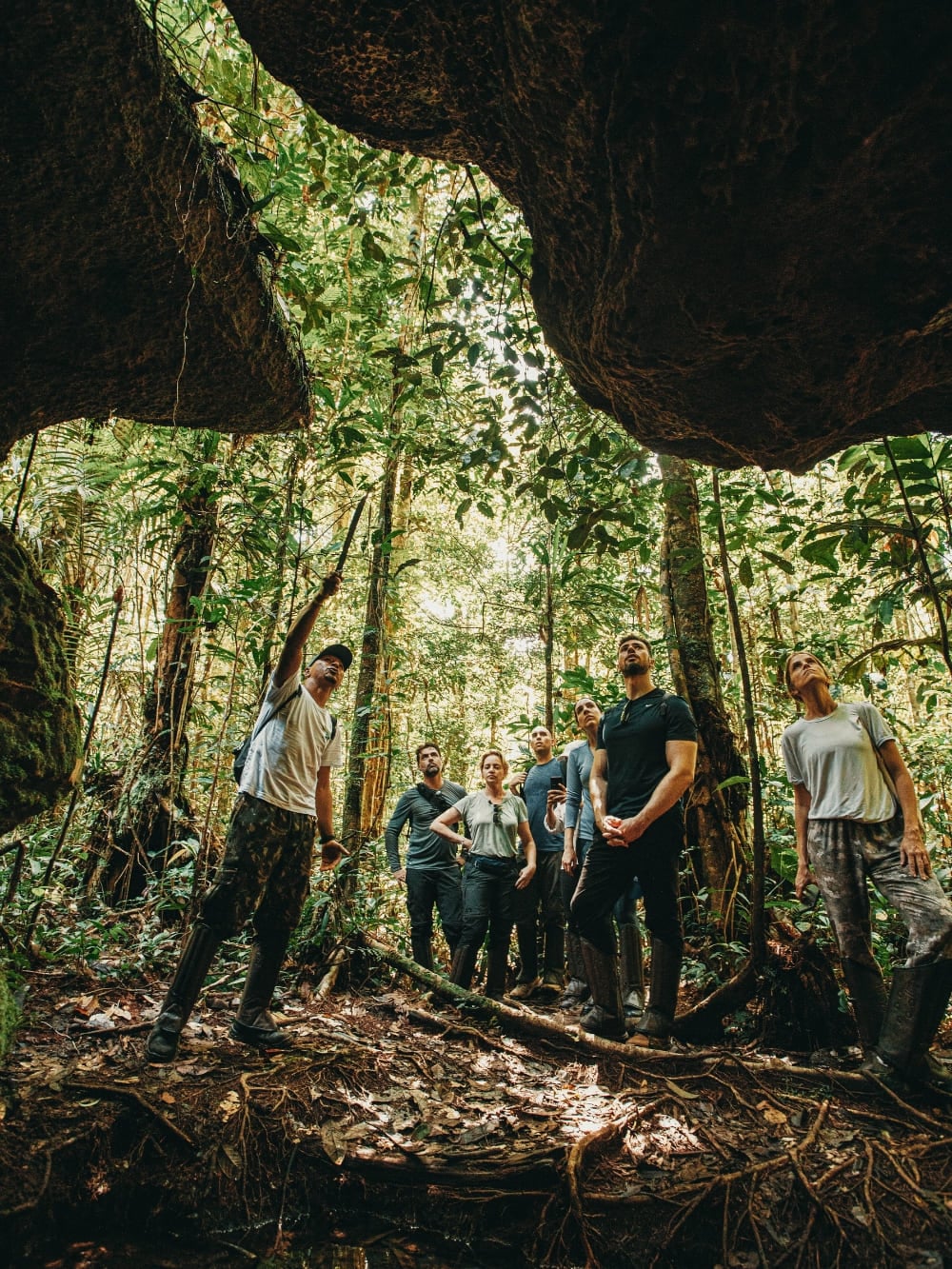 Group of tourists exploring a cave formation within the Amazon rainforest, looking out at the jungle with an expert local guide. Group of tourists exploring a cave formation within the Amazon rainforest, looking out at the jungle with an expert local guide.