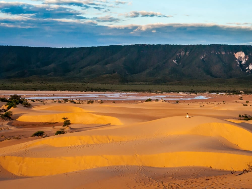 A traveler sits on the golden sand dunes of Jalapão watching the sunset over the mountains. A traveler sits on the golden sand dunes of Jalapão watching the sunset over the mountains.