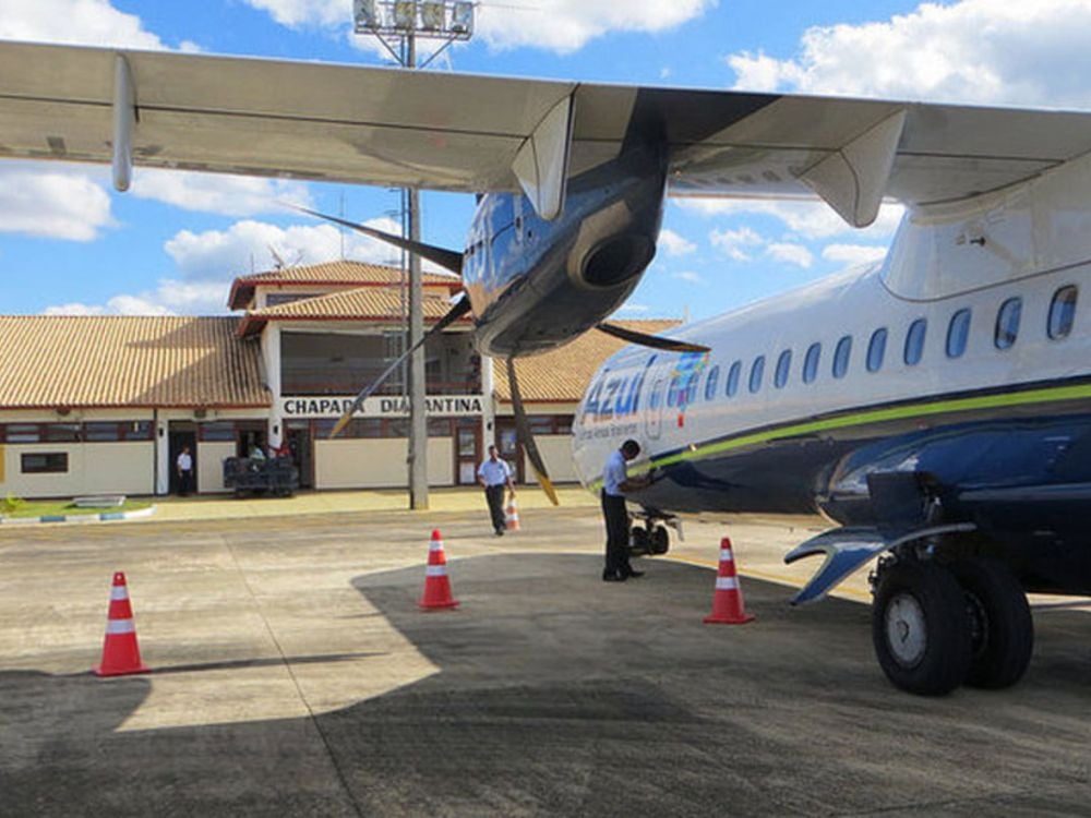 Azul airline plane parked on the runway at Chapada Diamantina airport. Employees work near the aircraft on a sunny day. Azul airline plane parked on the runway at Chapada Diamantina airport. Employees work near the aircraft on a sunny day.