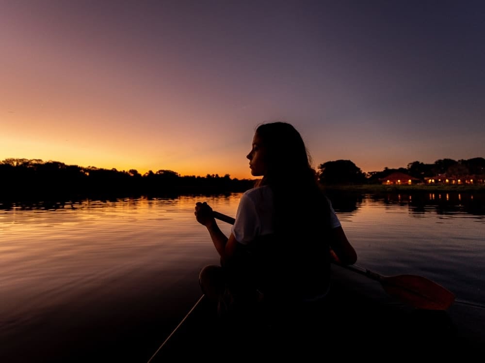 A woman paddling a canoe on a calm river at sunset, highlighting the peaceful nature of a Pantanal trip. A woman paddling a canoe on a calm river at sunset, highlighting the peaceful nature of a Pantanal trip.