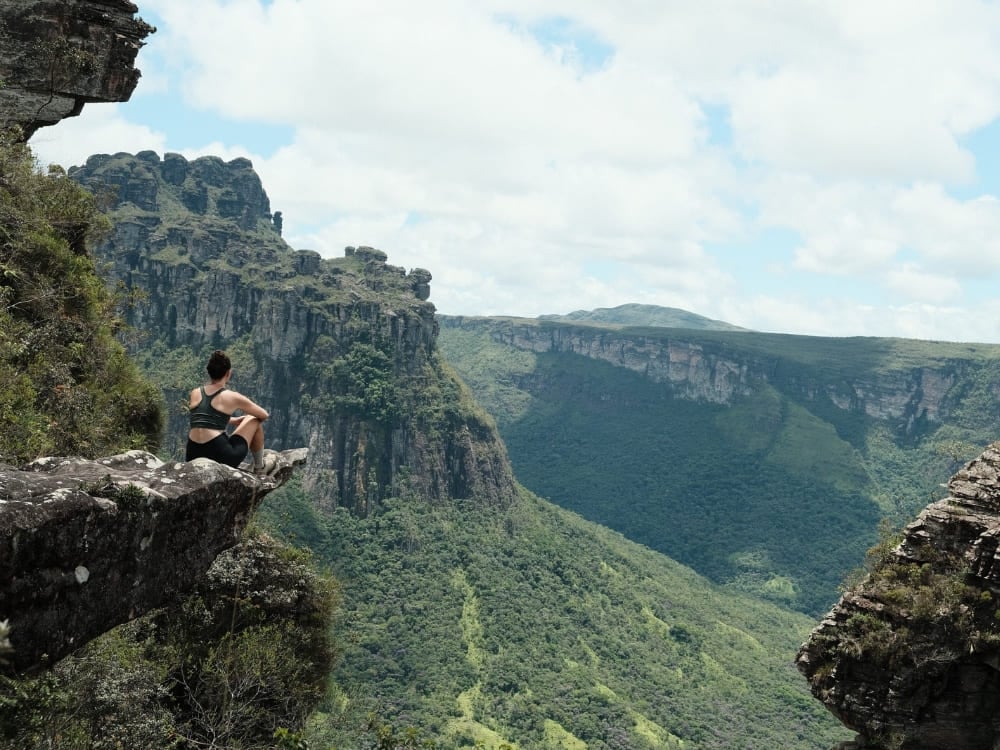 A person sits on a rocky cliff edge overlooking the deep, green forest canyons of Chapada Diamantina. A person sits on a rocky cliff edge overlooking the deep, green forest canyons of Chapada Diamantina.