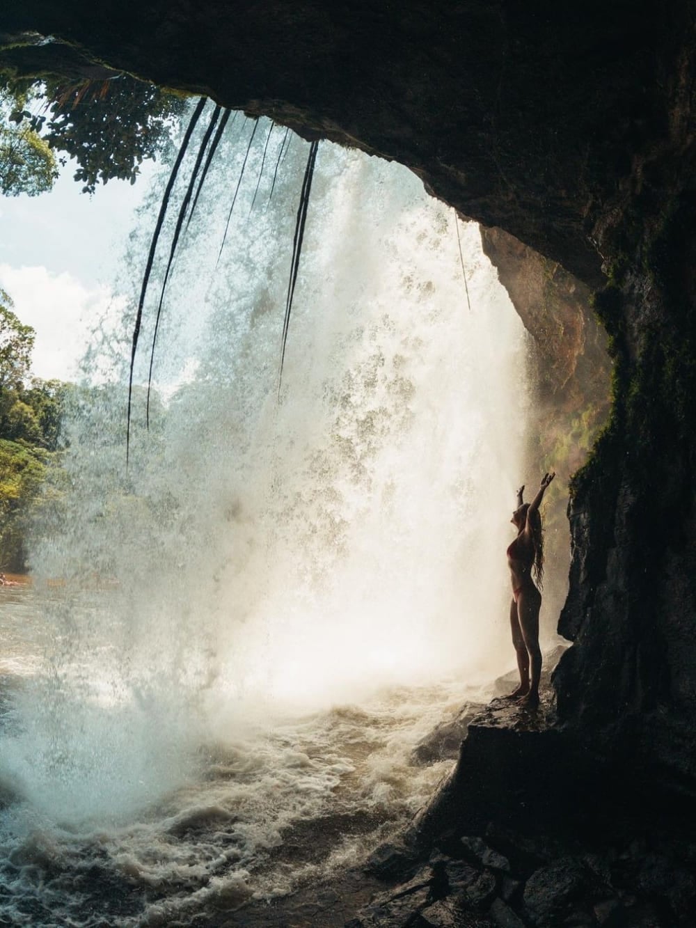 Silhouette of a woman with open arms contemplating a strong waterfall from the dark interior of a cave. Silhouette of a woman with open arms contemplating a strong waterfall from the dark interior of a cave.