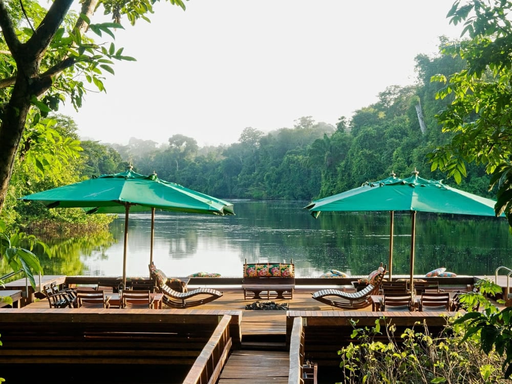Wooden deck with green umbrellas and lounge chairs overlooking a serene Amazon river. Wooden deck with green umbrellas and lounge chairs overlooking a serene Amazon river.