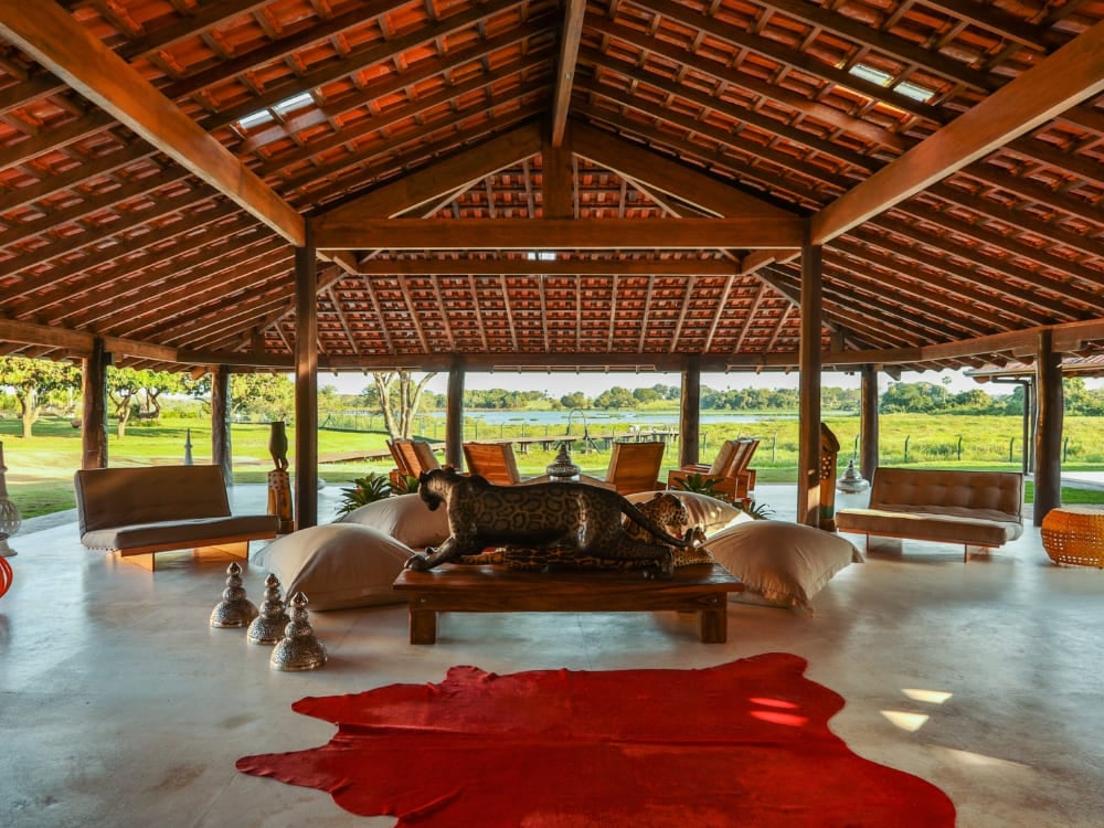 Open-air living room featuring a red cowhide rug and a carved wooden jaguar at Caiman ecolodge. Open-air living room featuring a red cowhide rug and a carved wooden jaguar at Caiman ecolodge.