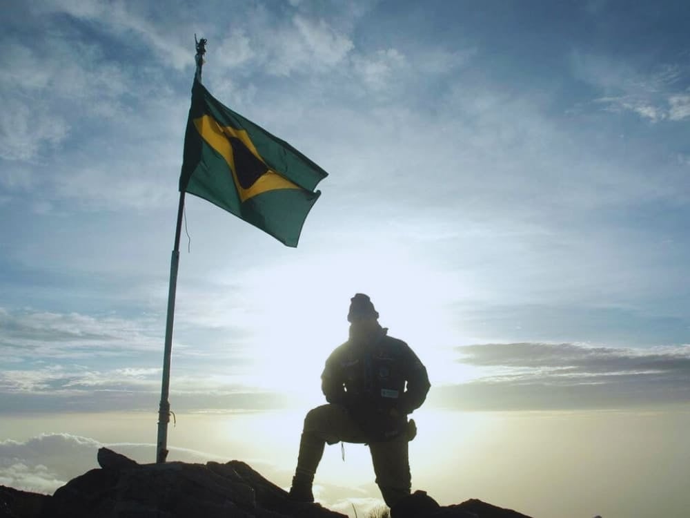 Silhouette of an explorer kneeling next to a waving Brazilian flag at the summit of Pico da Neblina at sunrise. Silhouette of an explorer kneeling next to a waving Brazilian flag at the summit of Pico da Neblina at sunrise.