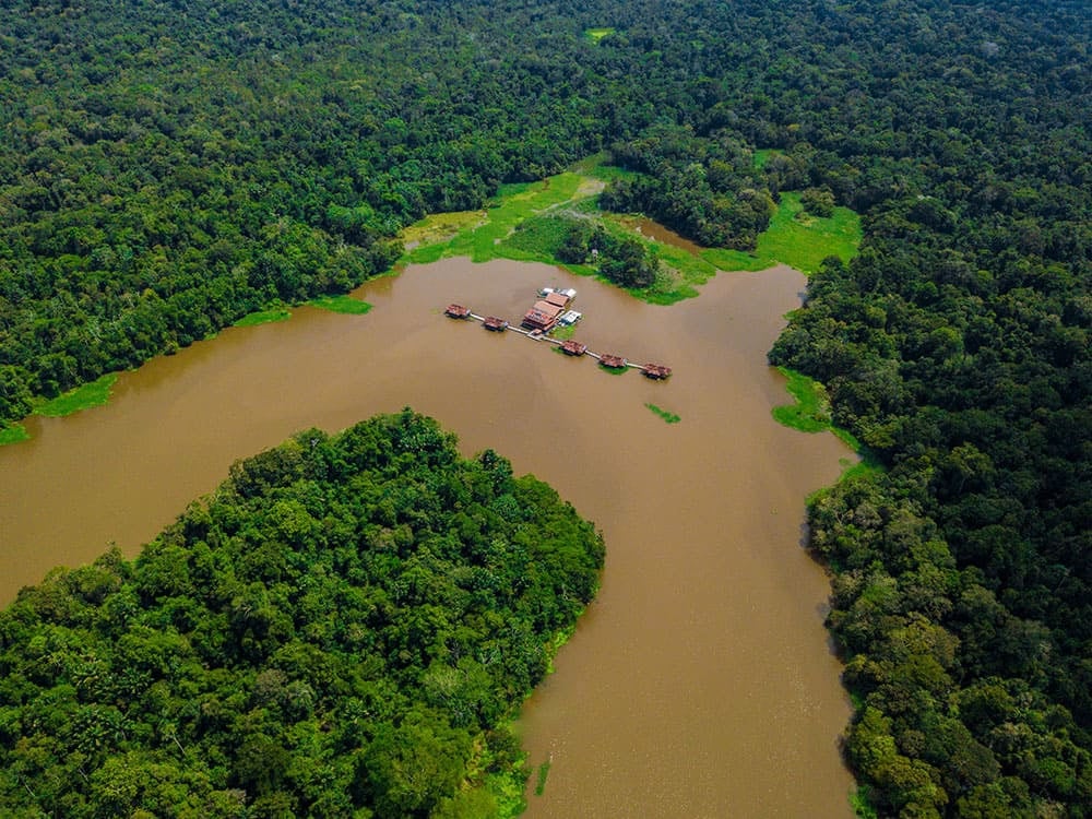 Aerial view of an eco-lodge with floating structures on a winding river completely surrounded by dense forest. Aerial view of an eco-lodge with floating structures on a winding river completely surrounded by dense forest.