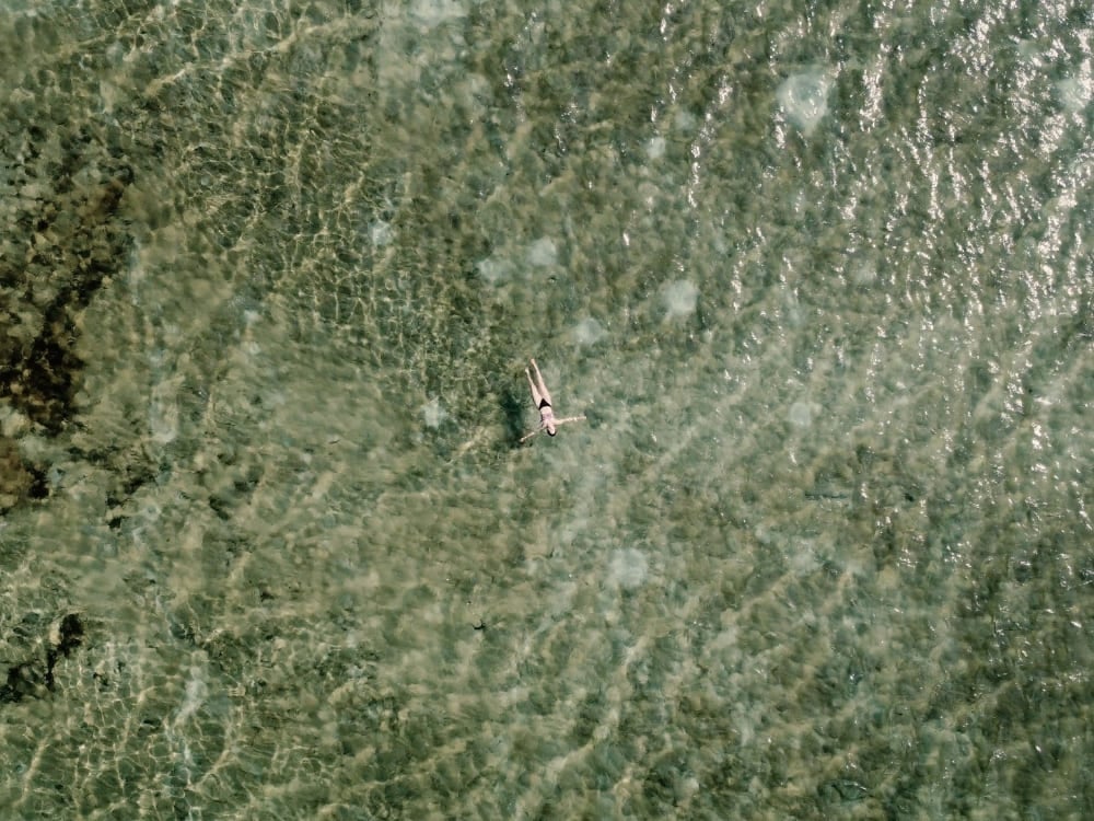 Top-down view of a person swimming in crystal-clear, shallow water over a textured sandy bottom during a Lençóis Maranhenses tour. Top-down view of a person swimming in crystal-clear, shallow water over a textured sandy bottom during a Lençóis Maranhenses tour.