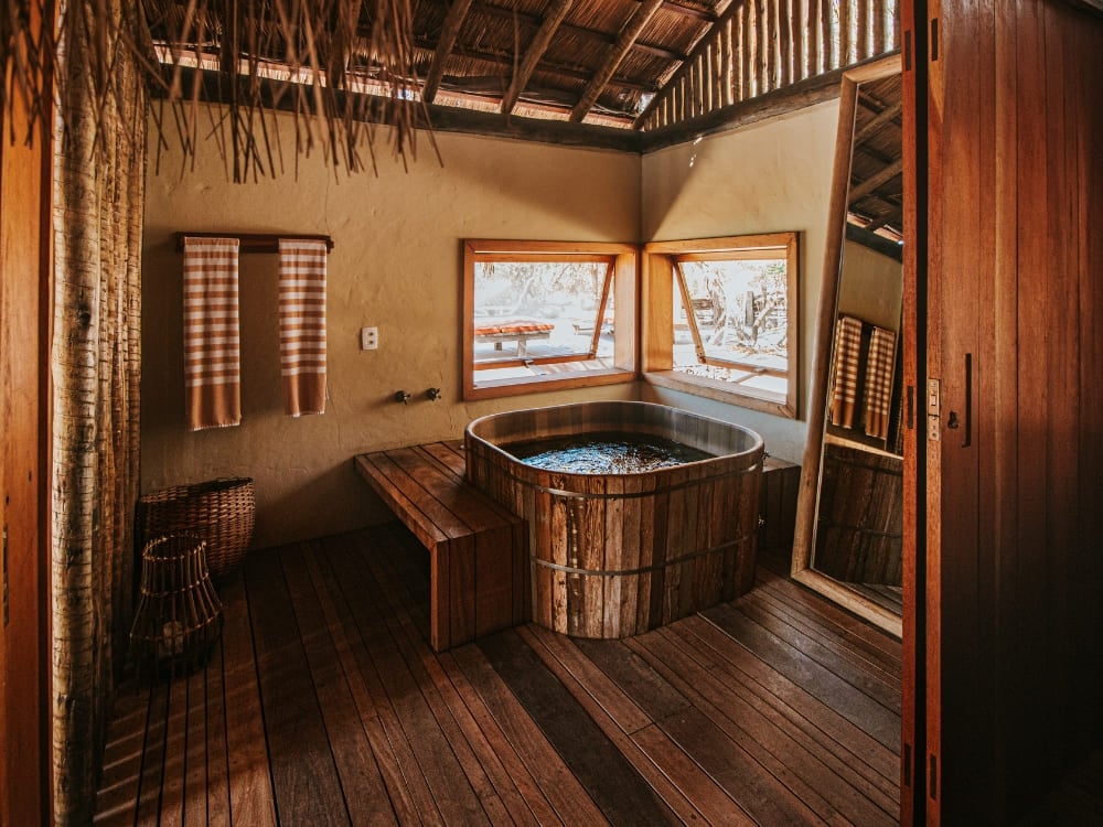 Wooden soaking tub set beside large windows inside a rustic suite at Pousada Trijuncao. Wooden soaking tub set beside large windows inside a rustic suite at Pousada Trijuncao.