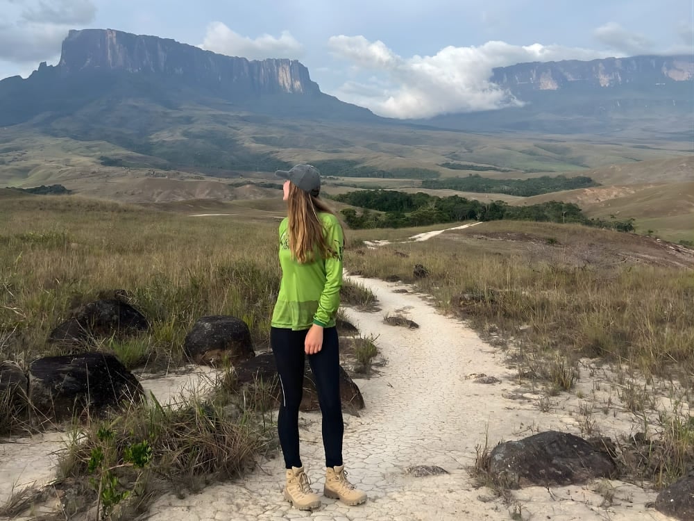 Female ecotourist standing on a dirt hiking trail with the stunning natural wonder of Mount Roraima in the background. Female ecotourist standing on a dirt hiking trail with the stunning natural wonder of Mount Roraima in the background.