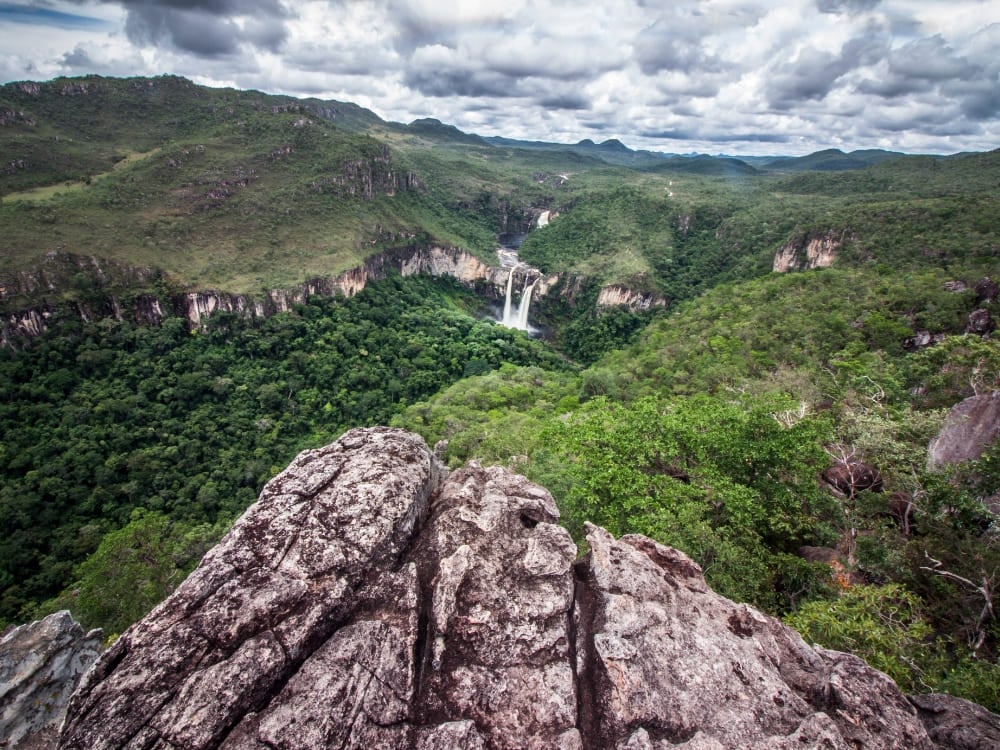 View from a rocky overlook showing a distant waterfall and lush vegetation in Chapada dos Veadeiros National Park. View from a rocky overlook showing a distant waterfall and lush vegetation in Chapada dos Veadeiros National Park.
