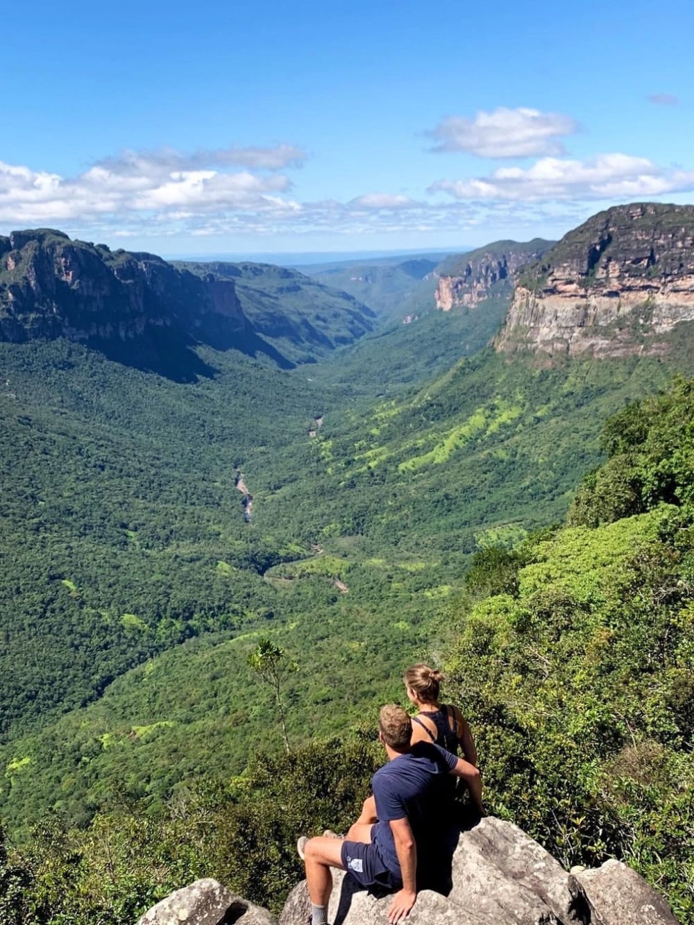 Two hikers sit on a rocky cliff admiring the vast, green expanse of Vale do Pati in Chapada Diamantina National Park. Two hikers sit on a rocky cliff admiring the vast, green expanse of Vale do Pati in Chapada Diamantina National Park.