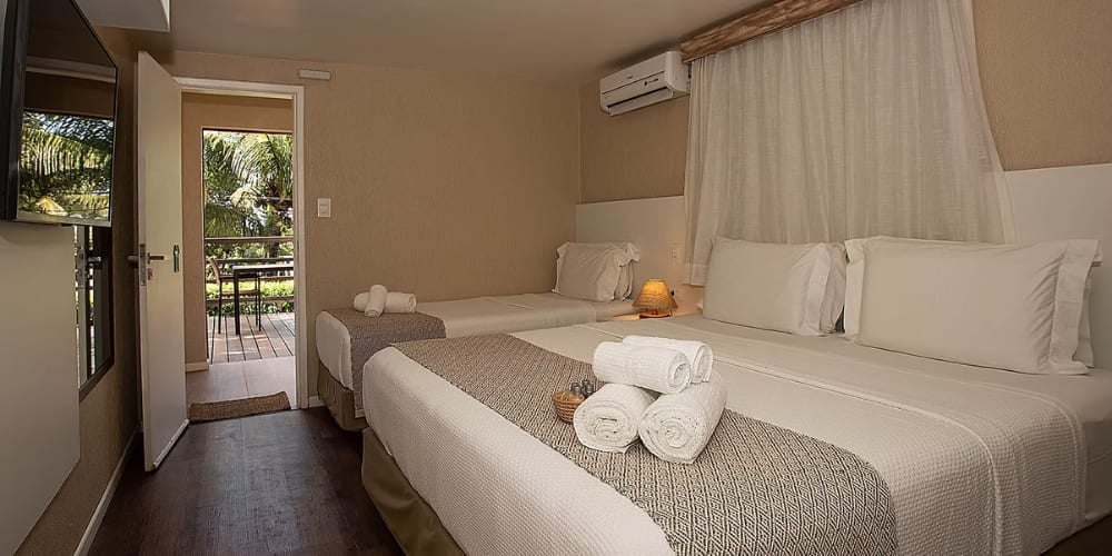 Cozy hotel room featuring a double bed, a single bed, and an open doorway leading to a sunny outdoor balcony in a Fernando de Noronha accommodation. Cozy hotel room featuring a double bed, a single bed, and an open doorway leading to a sunny outdoor balcony in a Fernando de Noronha accommodation.