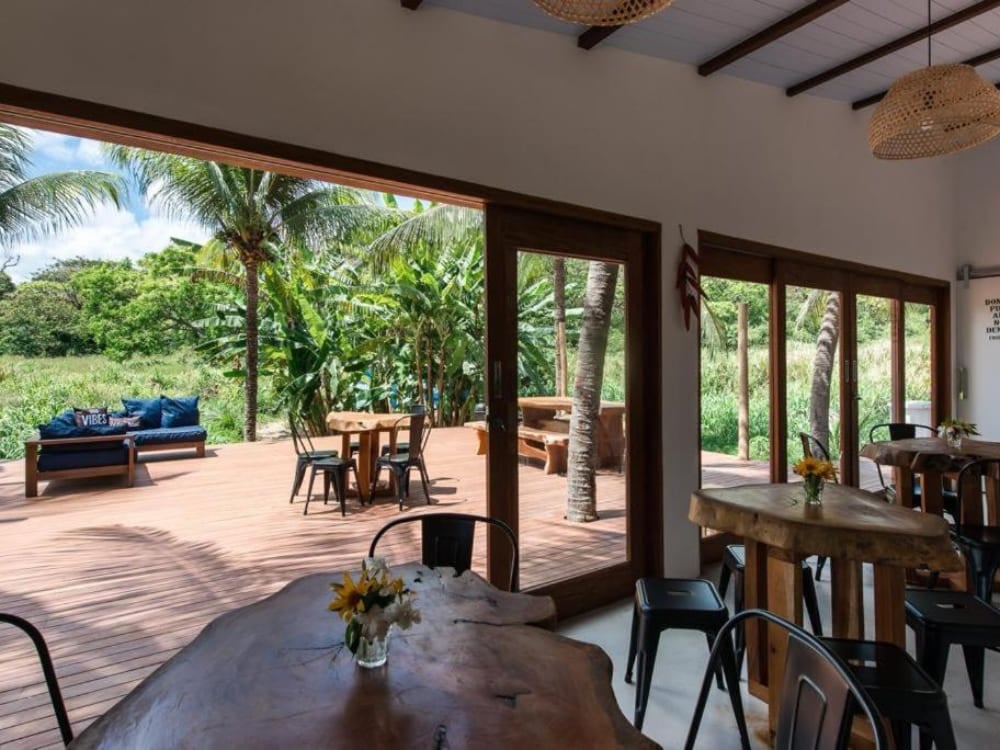 Open-air common area of a hostel with a rustic wooden table and wide doors showing lush vegetation in Fernando de Noronha. Open-air common area of a hostel with a rustic wooden table and wide doors showing lush vegetation in Fernando de Noronha.