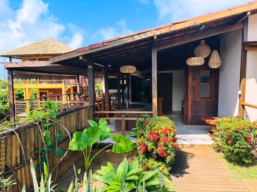 Charming guesthouse exterior featuring a covered porch, wooden pillars, and a green tropical garden in Fernando de Noronha. Charming guesthouse exterior featuring a covered porch, wooden pillars, and a green tropical garden in Fernando de Noronha.