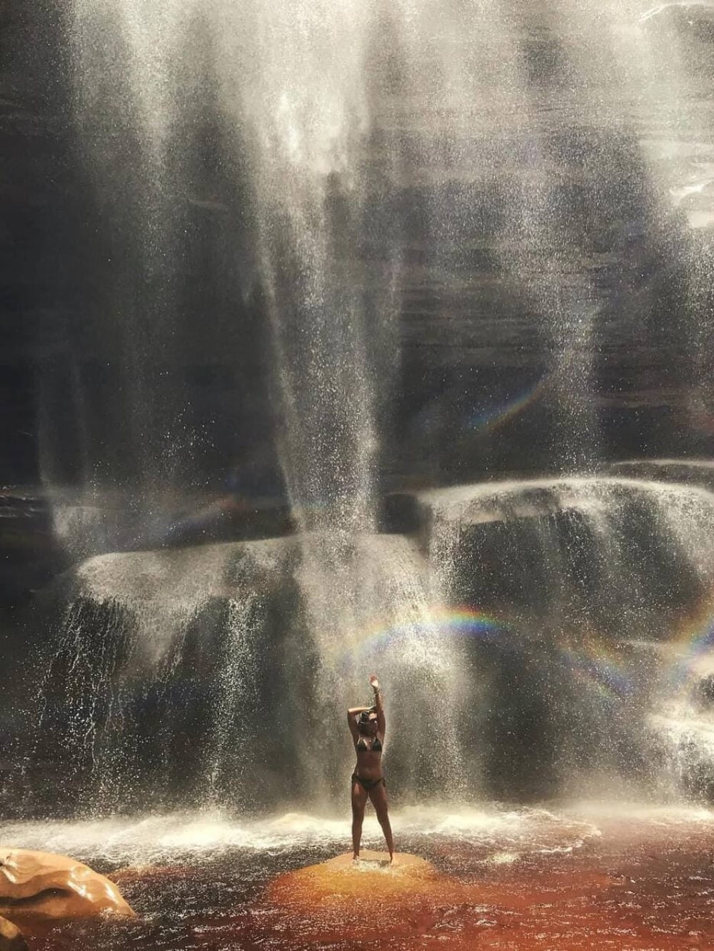 A woman stands on a rock stretching her arms at the base of the 60-meter Mosquito Waterfall, surrounded by a wide swimming pool. A woman stands on a rock stretching her arms at the base of the 60-meter Mosquito Waterfall, surrounded by a wide swimming pool.