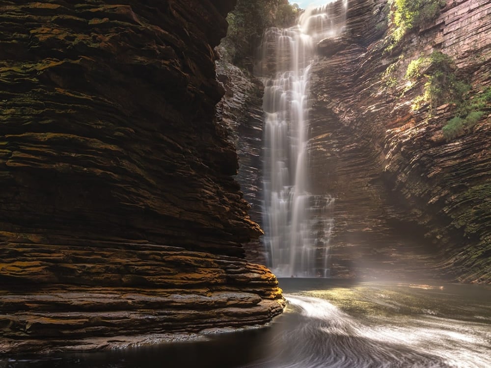 Buracão Waterfall drops 85 meters inside a narrow rocky canyon with layered walls, ending in a dark natural pool. Buracão Waterfall drops 85 meters inside a narrow rocky canyon with layered walls, ending in a dark natural pool.