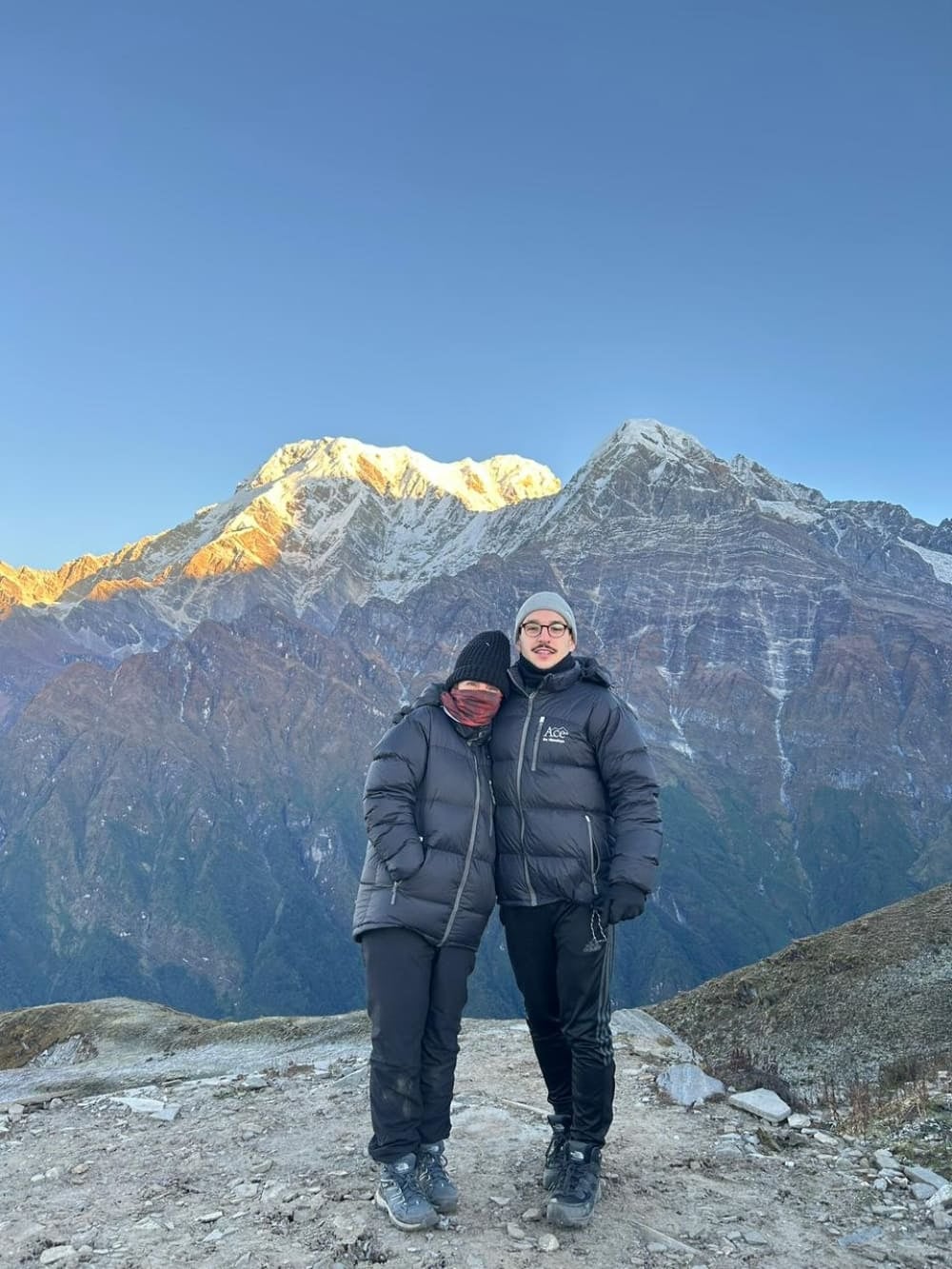 Mother and son Mila and Lorenzo wearing heavy winter gear and embracing in front of the snowy Himalayan peaks after an early morning climb. Mother and son Mila and Lorenzo wearing heavy winter gear and embracing in front of the snowy Himalayan peaks after an early morning climb.