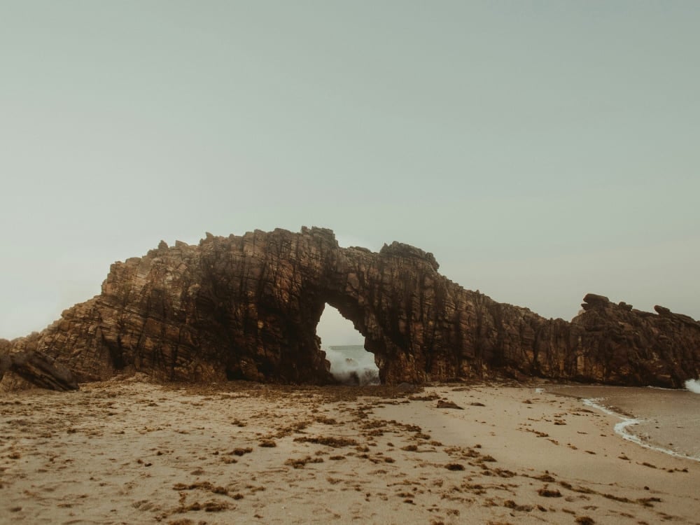 A large, rugged rock formation featuring a natural arch on a sandy beach beside the ocean, known as Pedra Furada in Jericoacoara. A large, rugged rock formation featuring a natural arch on a sandy beach beside the ocean, known as Pedra Furada in Jericoacoara.