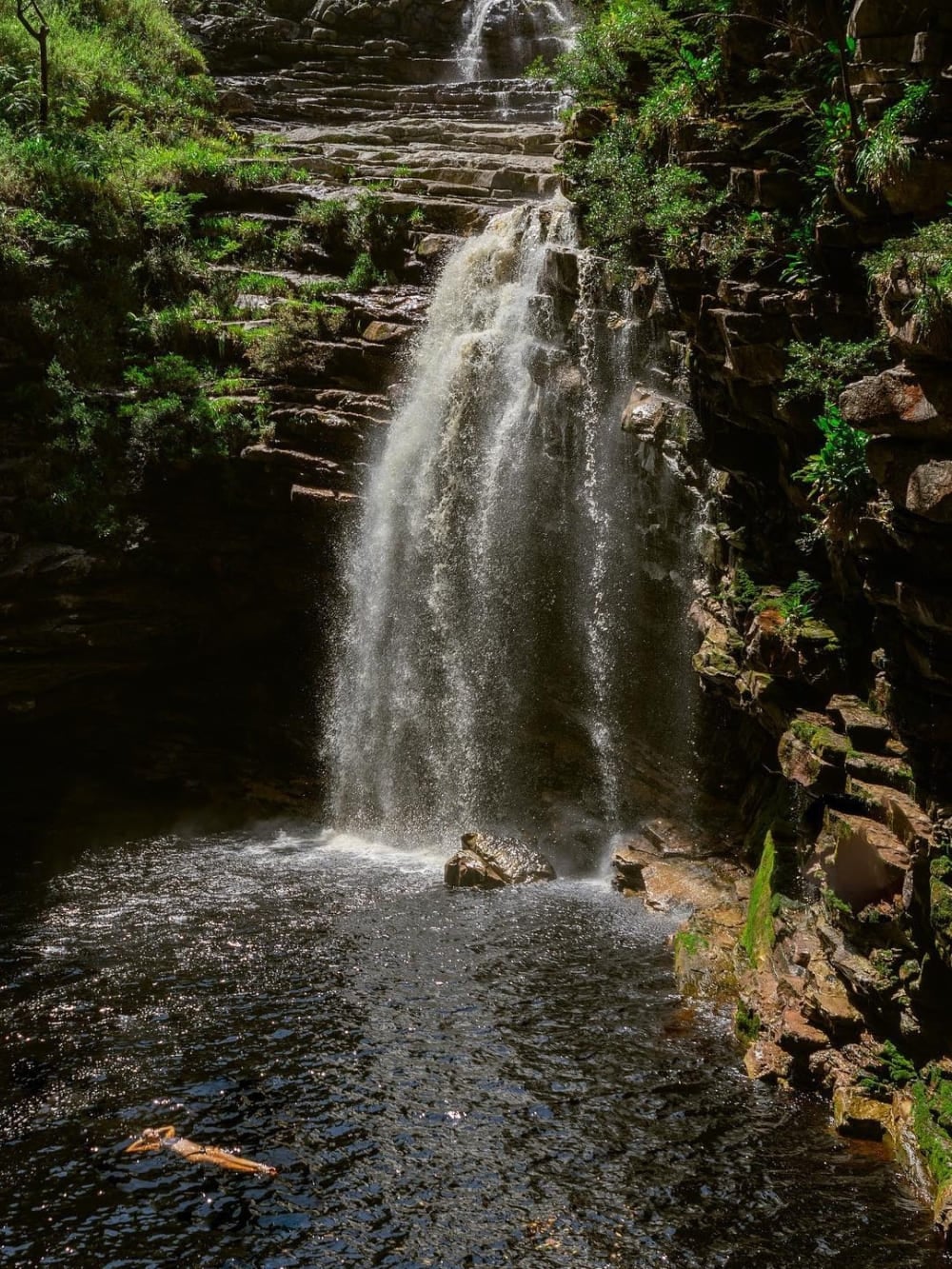 A person swims in the peaceful, dark natural pool at the base of the 20-meter Sossego Waterfall near Lençóis. A person swims in the peaceful, dark natural pool at the base of the 20-meter Sossego Waterfall near Lençóis.