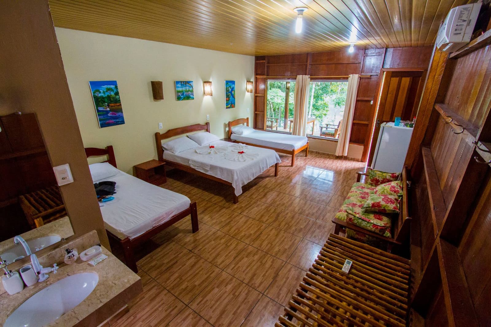 Comfortable and clean, with the jungle just outside the window. Spacious triple room at Amazon Turtle Lodge with three wooden-framed beds dressed in white linen, tropical artwork on cream walls, a bamboo ceiling fan, tiled floors, and a window opening onto lush rainforest canopy
