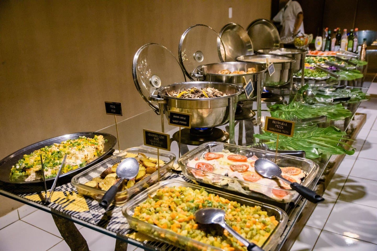 Turns out you work up quite an appetite after a day of wildlife watching. A wide lodge dinner buffet spread for a budget Pantanal tour, with labeled dishes including sweet potato, aubergine pizza, mixed vegetables, fish, and fresh salads kept warm in chafing dishes