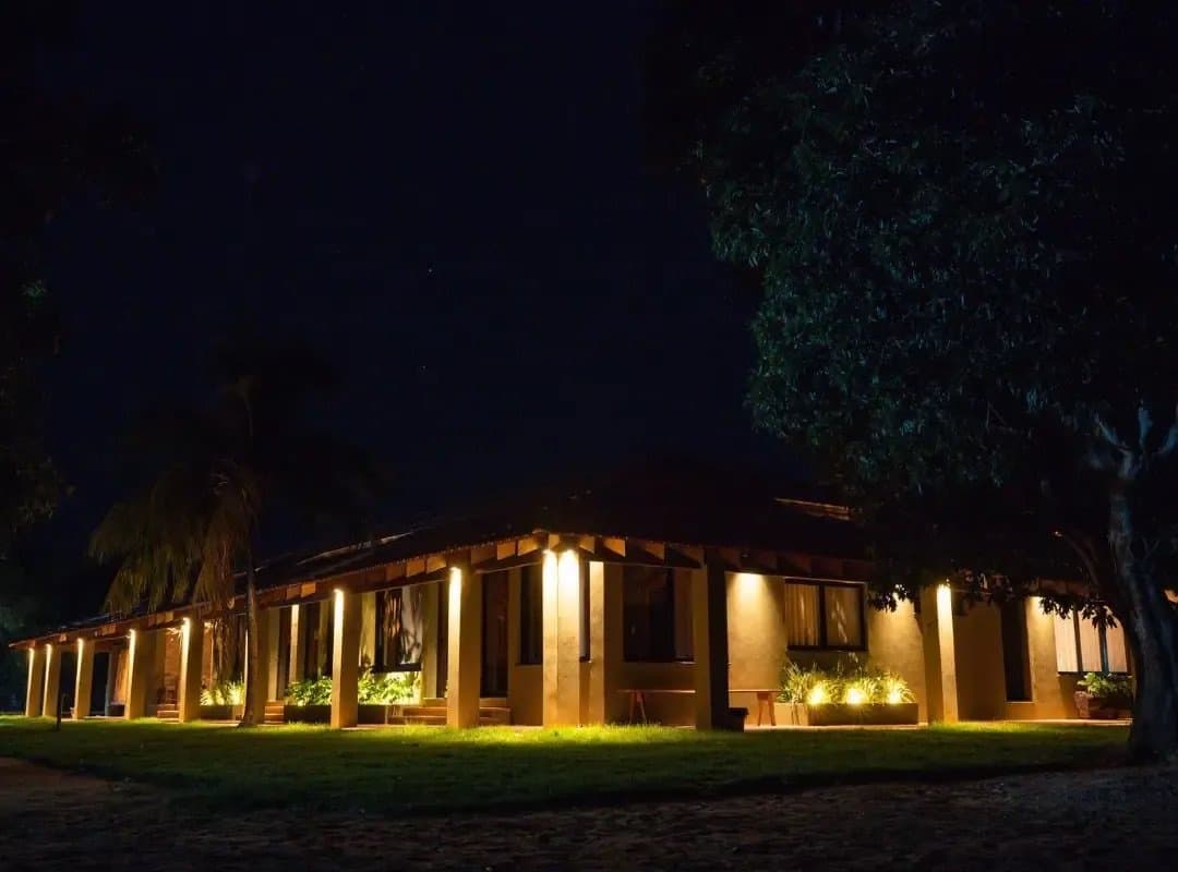 The kind of place that looks even better after a long day in the field. A low-slung ranch-style lodge glowing under warm golden lights at night, surrounded by lawns and trees on a southern pantanal safari stay