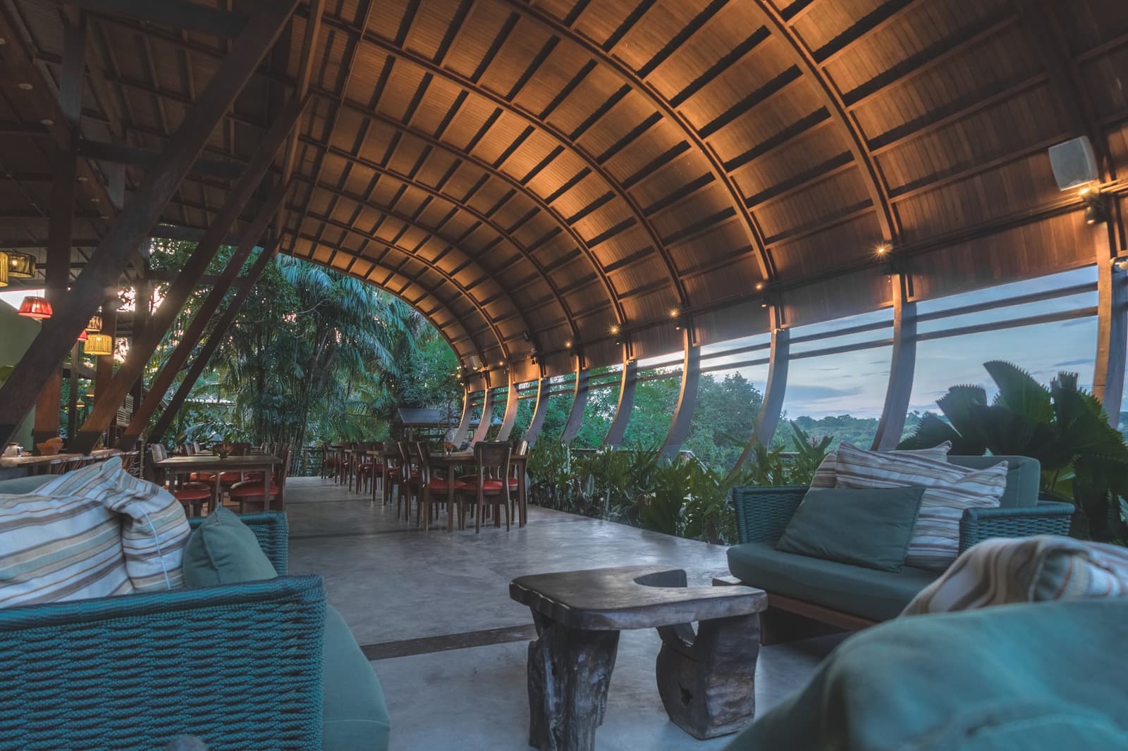 The kind of place where you forget to check your phone. The open-sided restaurant at Mirante do Gavião amazon lodge features a sweeping curved wooden ceiling, rattan lounge seating, and floor-to-ceiling views of the surrounding rainforest canopy at dusk