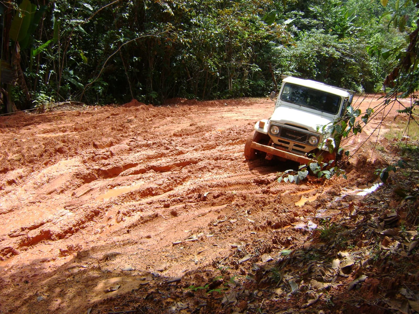 Mud this thick has its own personality, and it rarely cooperates. A white 4x4 vehicle navigating a deeply rutted red mud trail through dense tropical rainforest on the Pico da Neblina Expedition