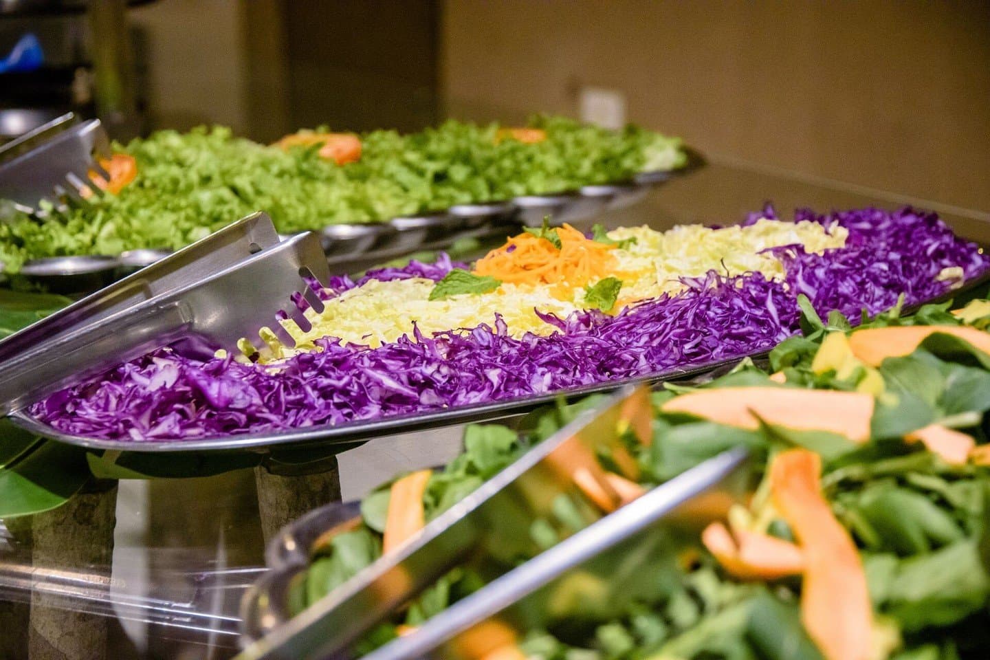 Eating well in the wild starts here. A buffet spread on a budget pantanal tour showing shredded red and white cabbage, grated carrot, fresh spinach, and melon slices arranged in large stainless-steel serving trays