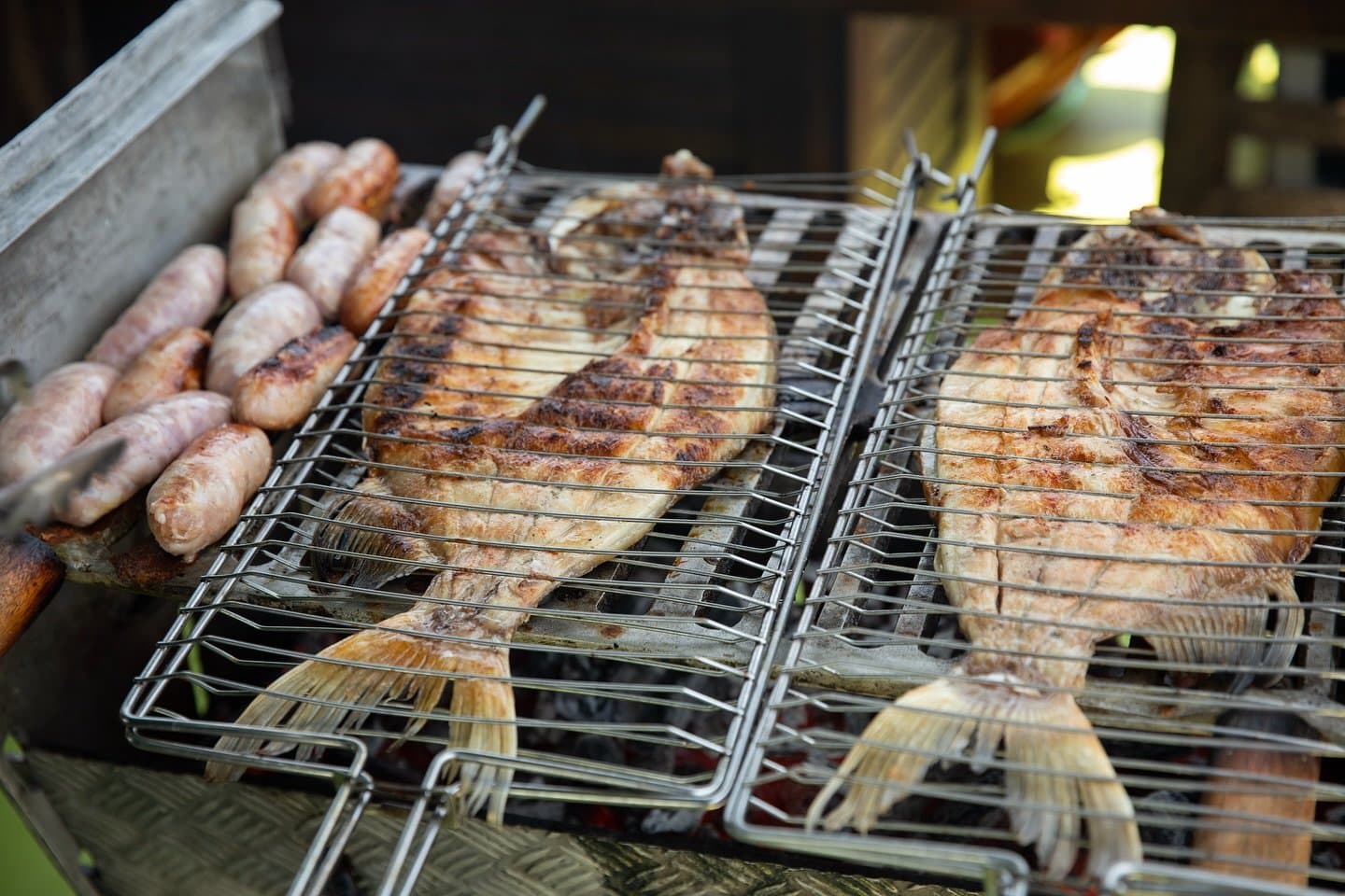 Fresh from the river to the grill, no detours. Whole fish with char marks clamped in wire grilling baskets alongside fresh sausages on a charcoal barbecue grill, served on an Amazon cruise trip in Brazil
